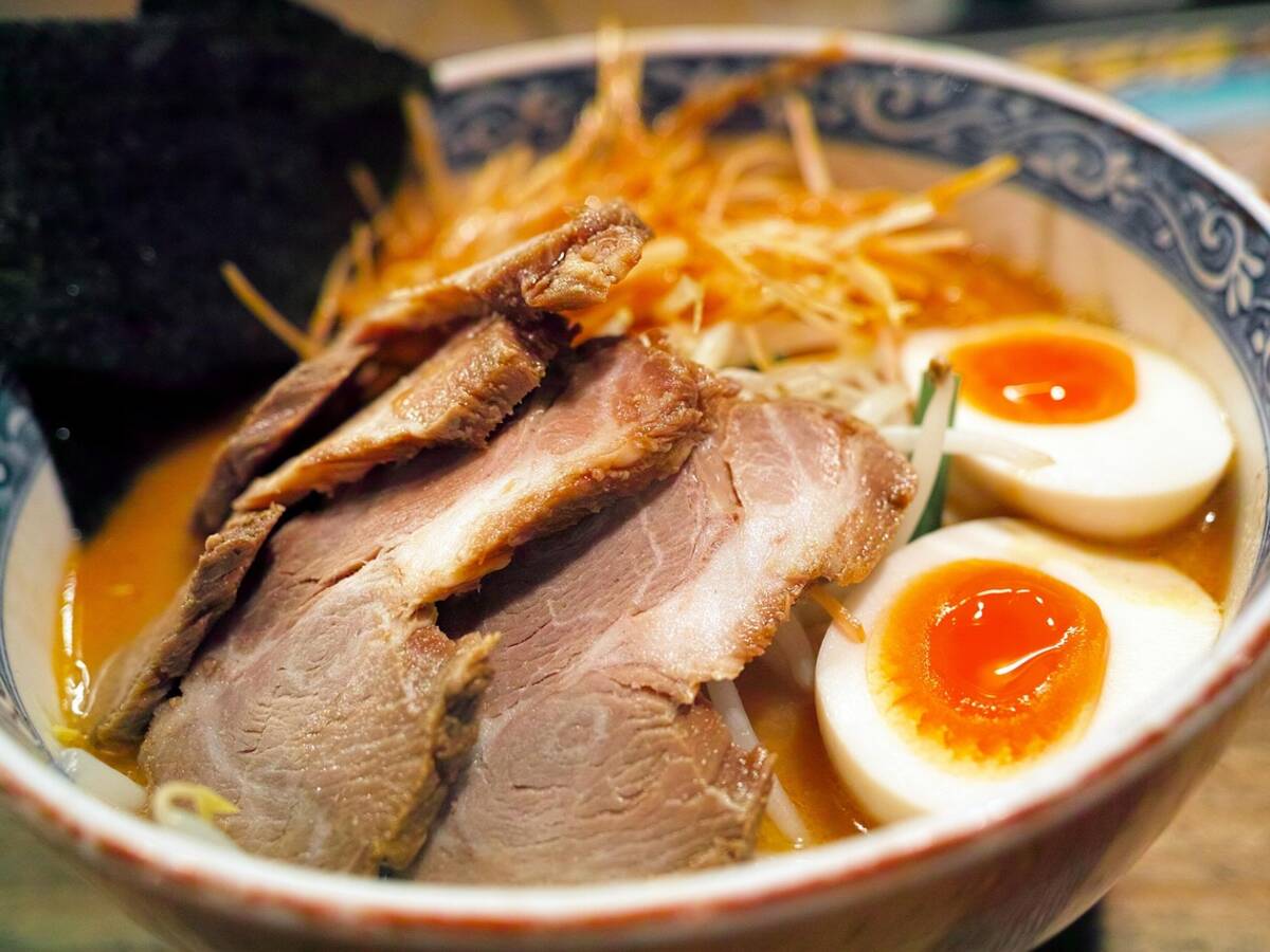 Bol de ramen fumant avec un œuf mollet, posé à côté d'une paire de baguettes